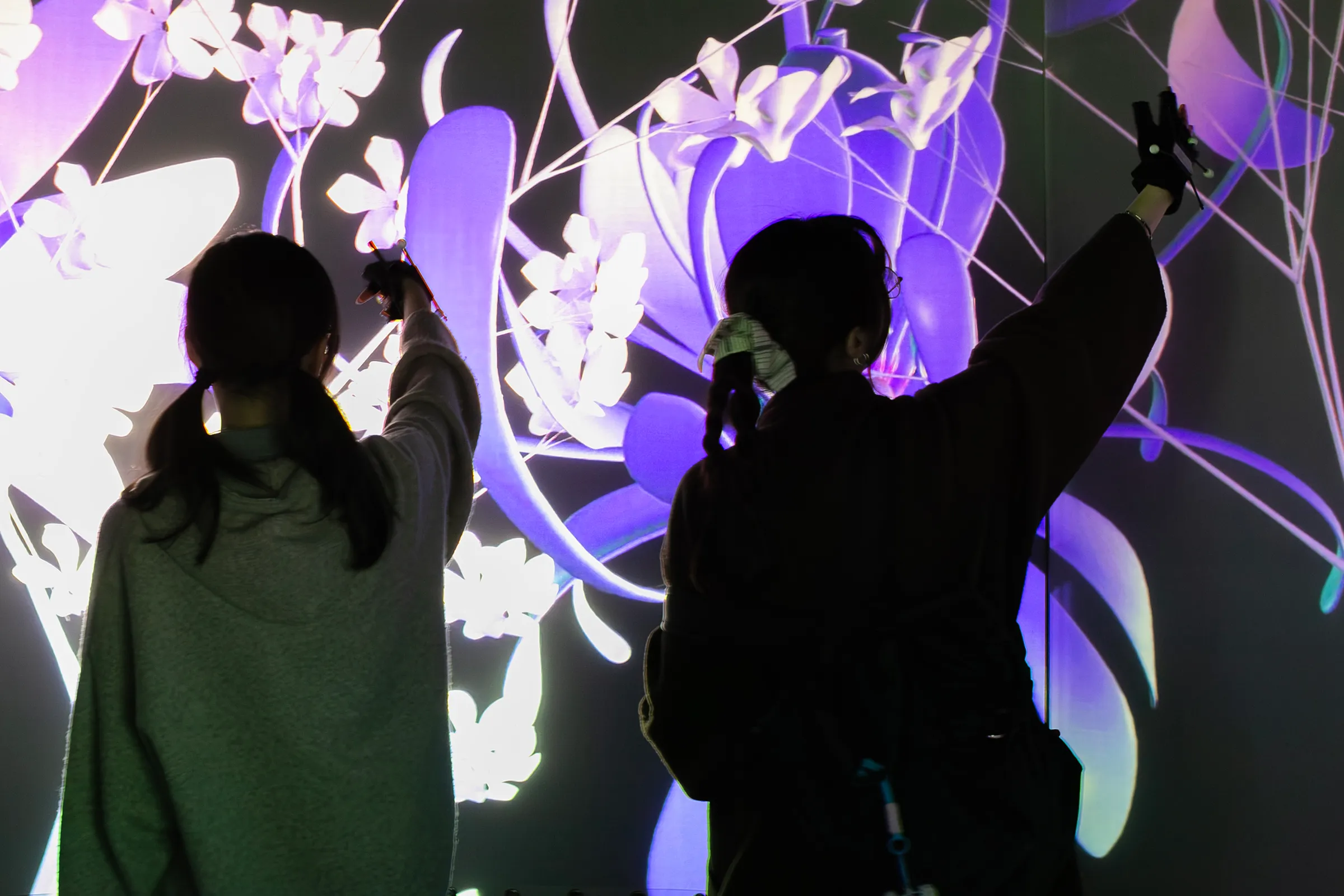 Two visitors raising their arms toward the projected flowers