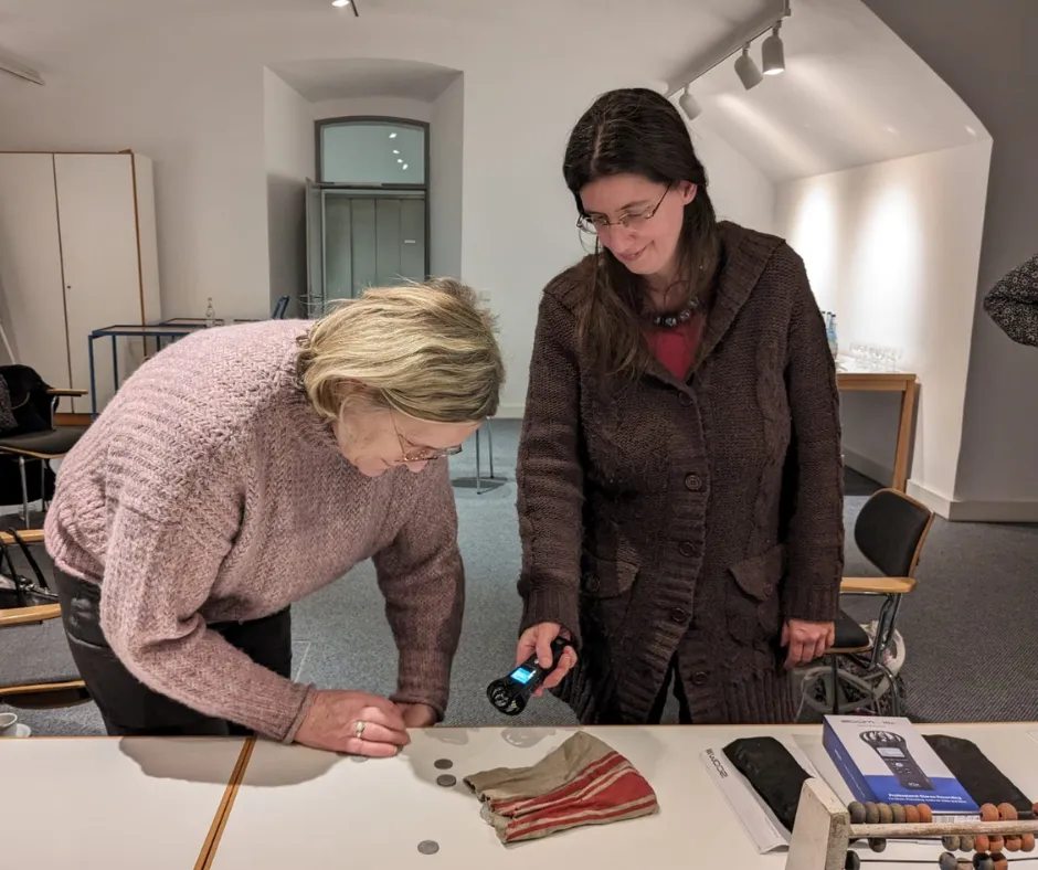 Two women recording the sound of coins with a handheld audio recorder