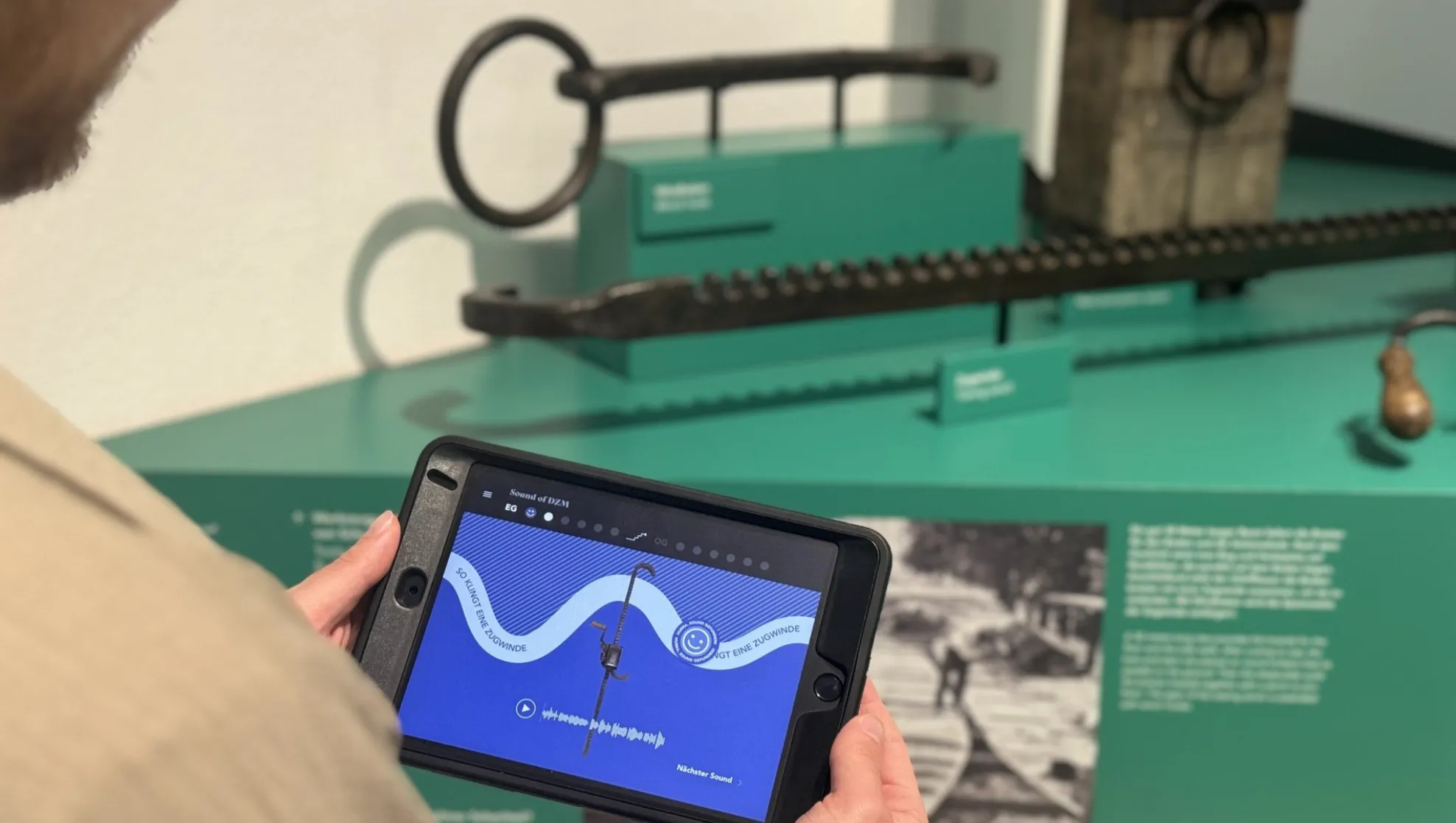 A visitor holding a tablet with the Sounds of DZM app in front of a historic winch in the exhibition