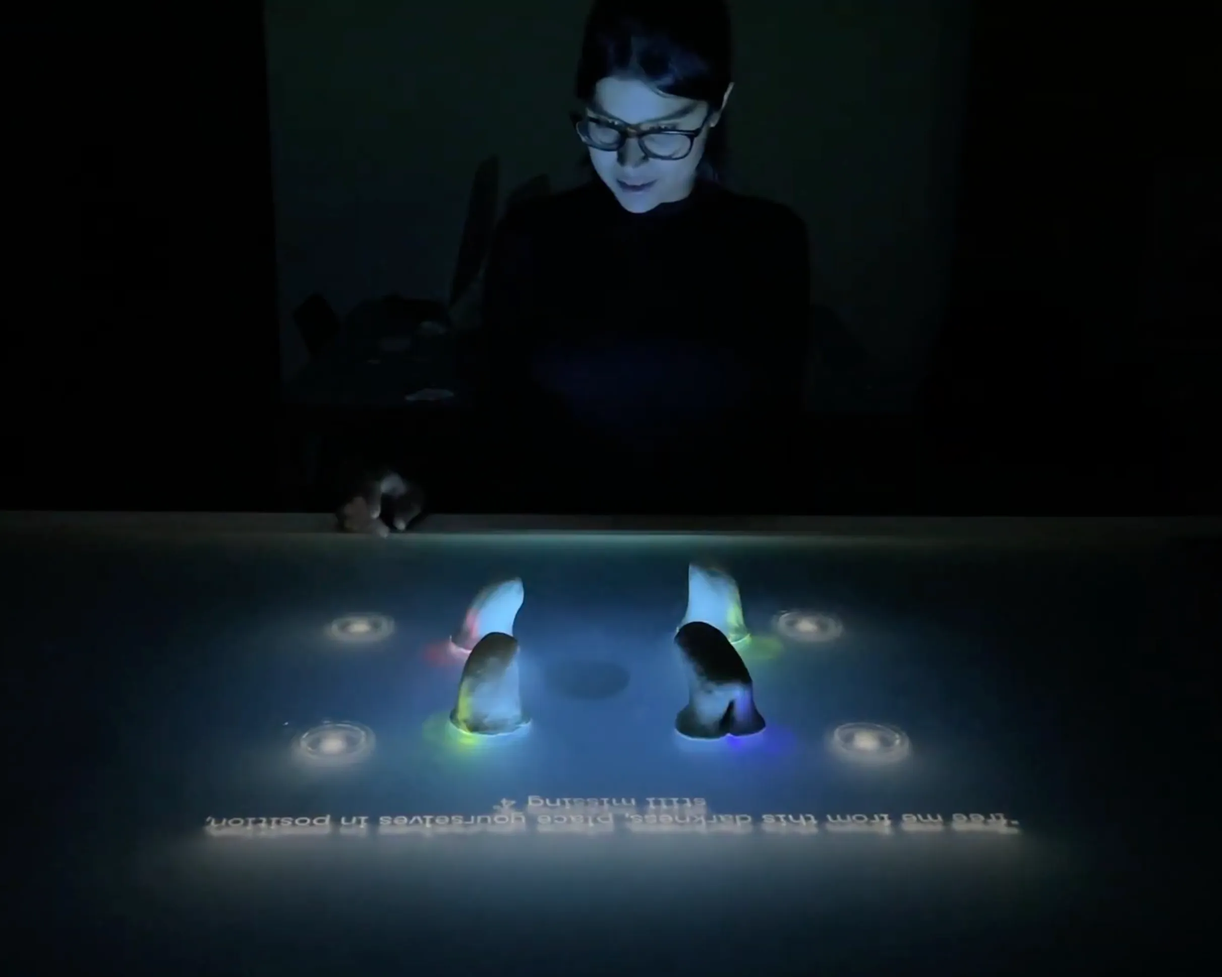 A player leaning over the dark interactive table, where glowing alien-shaped controllers stand among projected lights and lyrics